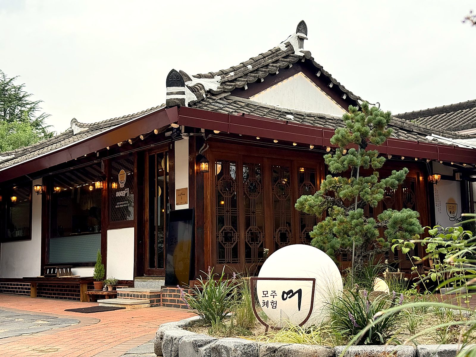 정원에서 본 모주체험 여 한옥 정면과 원반 간판 · The hanok front and round sign, seen from the garden