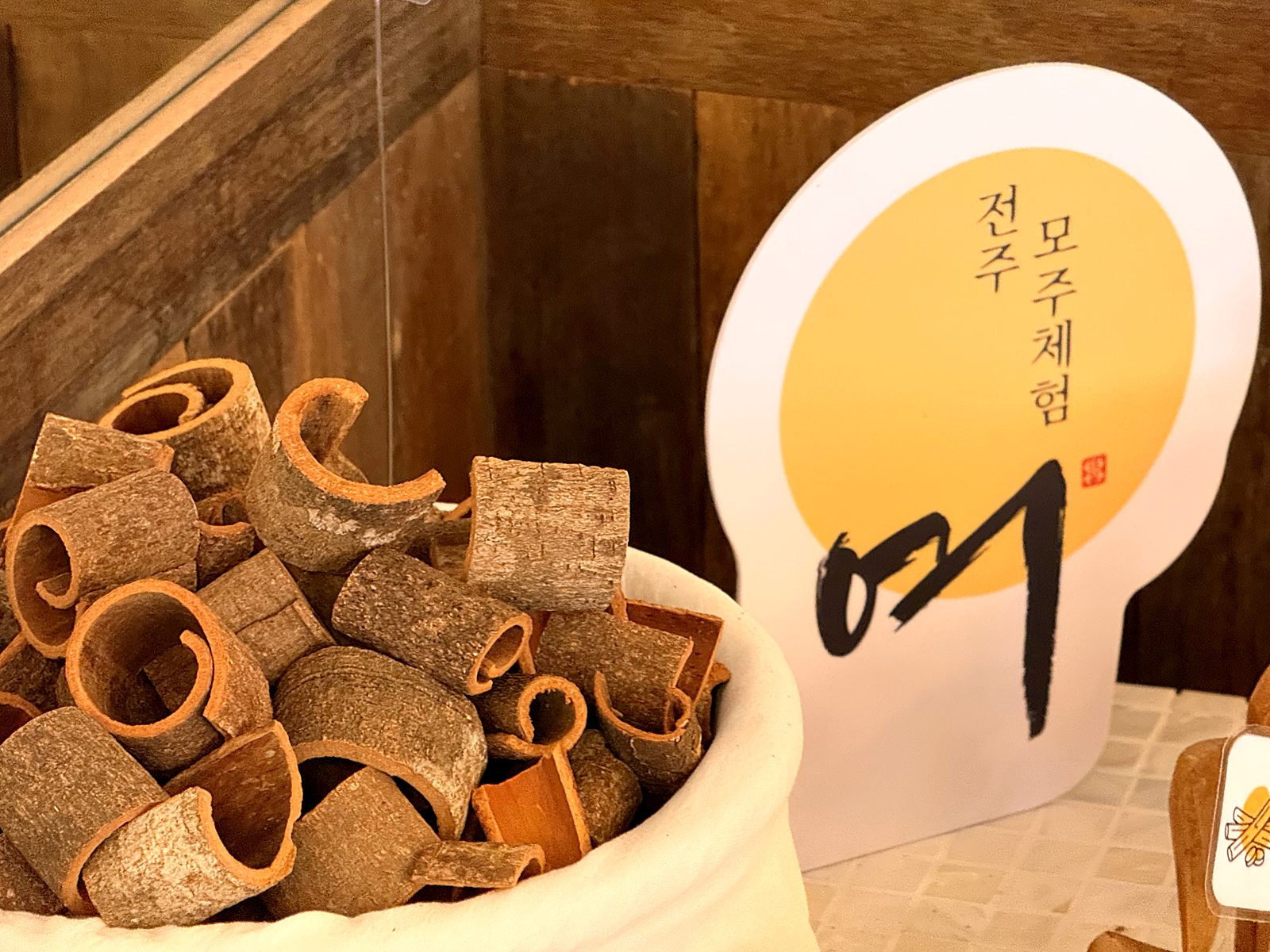 소쿠리에 담긴 계피 조각과 달 로고 스탠드 · Curled cinnamon bark in a basket beside the moon sign